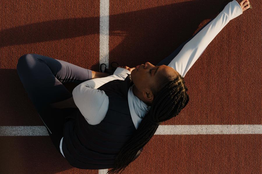 A runner stretches her legs and arms, leaning on her right, on the running tracks.