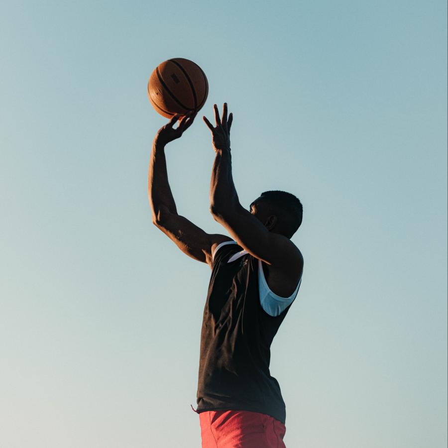 A basketball athlete jumps while shooting basketball at the hoop.