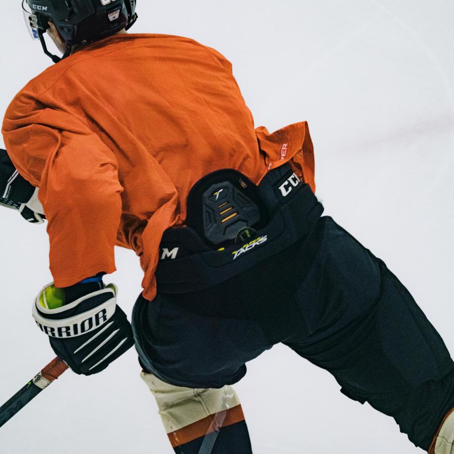 A hockey player is skating forward with his orange shirt tucked in the back.